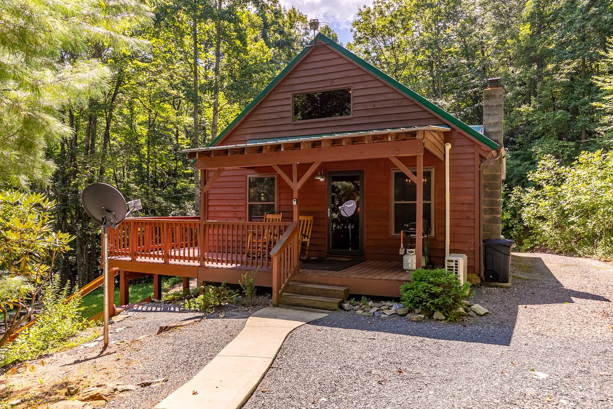 The hero image displays the charming wooden deck and front door of the Blue Flower Cabin, nestled among lush greenery on a private 10-acre lot. The inviting deck is perfect for relaxing, with scenic views of the surrounding forest and the promise of tranquil sunsets and starlit nights. The setting evokes a cozy, secluded escape, ideal for connecting with nature.