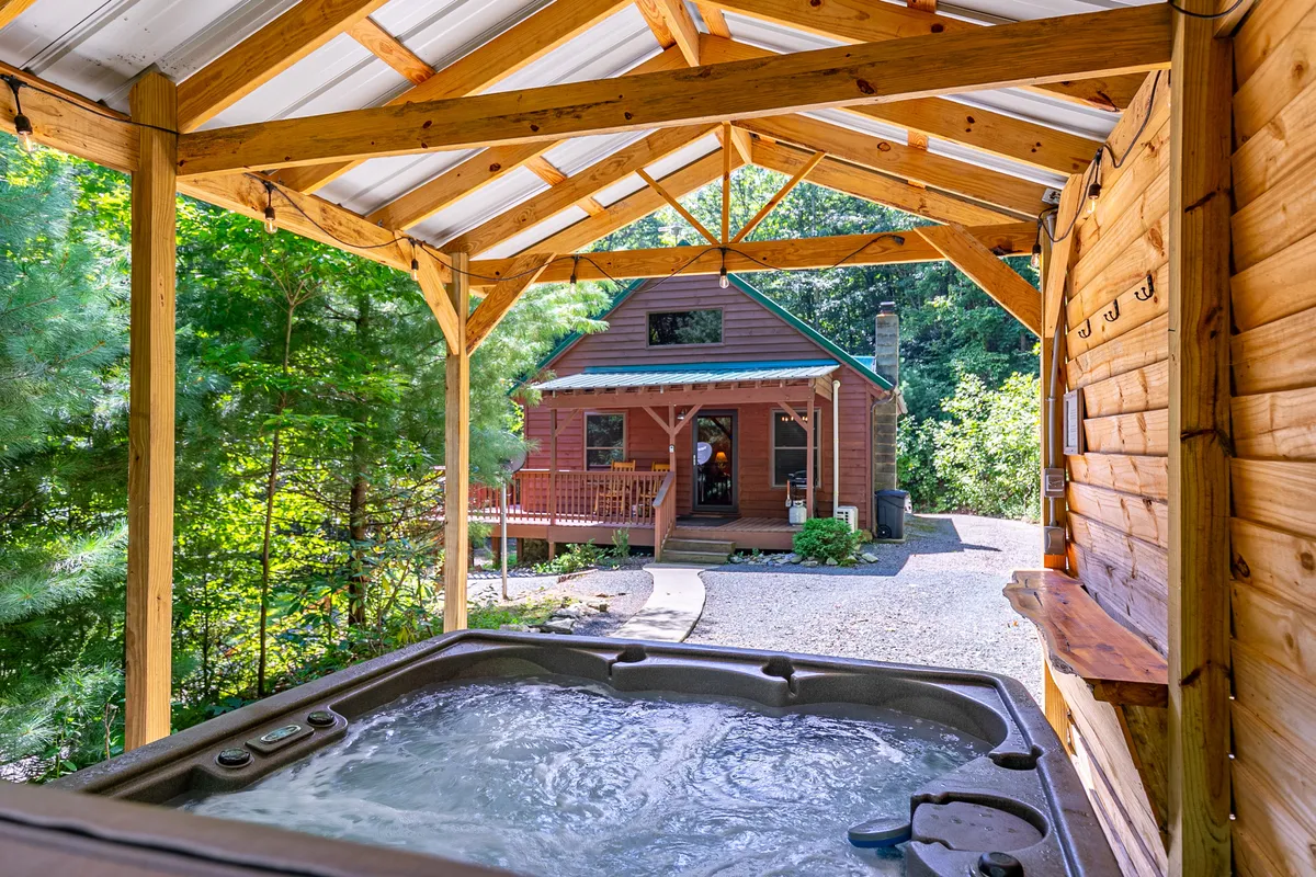 This tranquil exterior scene features a hot tub placed near the cabin, surrounded by trees for privacy. The inviting hot tub sits under open sky—an ideal spot for soaking while gazing at stars or relaxing after a day of mountain adventures. The cabin’s porch and natural surroundings create a rejuvenating, luxurious vibe.