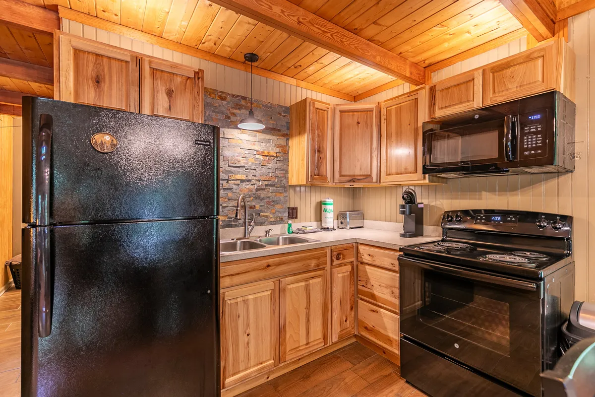 A close-up of the modern kitchen, featuring a black refrigerator, stone backsplash, wooden cabinetry, and stainless steel appliances. The layout is inviting and clearly shows the kitchen's functionality for both cooking and entertaining.