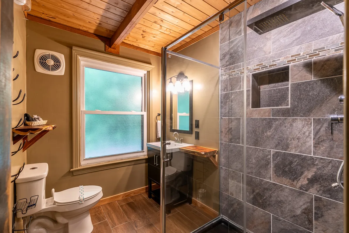 A modern glass-enclosed shower is showcased alongside a stylish wooden vanity and decorative lighting. The space feels calm and rejuvenating, with clean lines and thoughtful spa-like touches.