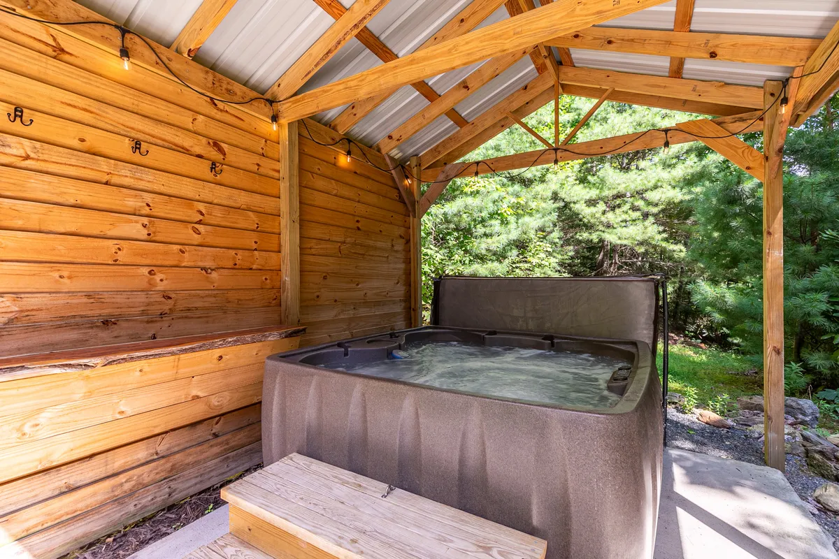 This image features a tranquil hot tub set against a wooden wall with a wooden bench nearby, inviting guests to relax and soak in nature. The setting hints at an outdoor connection, as the hot tub area is associated with stargazing and enjoying the surrounding nature, suggesting proximity to the scenic landscape described.