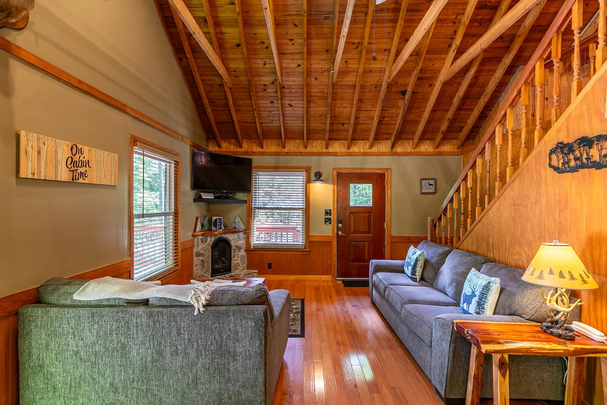 This inviting interior scene highlights plush sofas arranged around a wooden staircase and a stone fireplace, with decorative wall art and large windows letting in natural light. The setup suggests a space ideal for relaxation, social games, and storytelling, all central to family bonding during a rainy day.