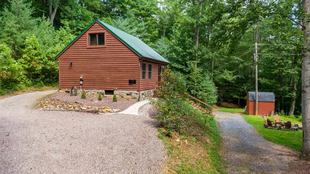 This exterior image showcases a charming wooden cabin set against a peaceful backdrop of surrounding trees. In the foreground, a clearly visible fire pit area suggests a space for outdoor gatherings, roasting marshmallows, and sharing stories under the stars. The secluded setting and open sky evoke a sense of serenity ideal for stargazing.