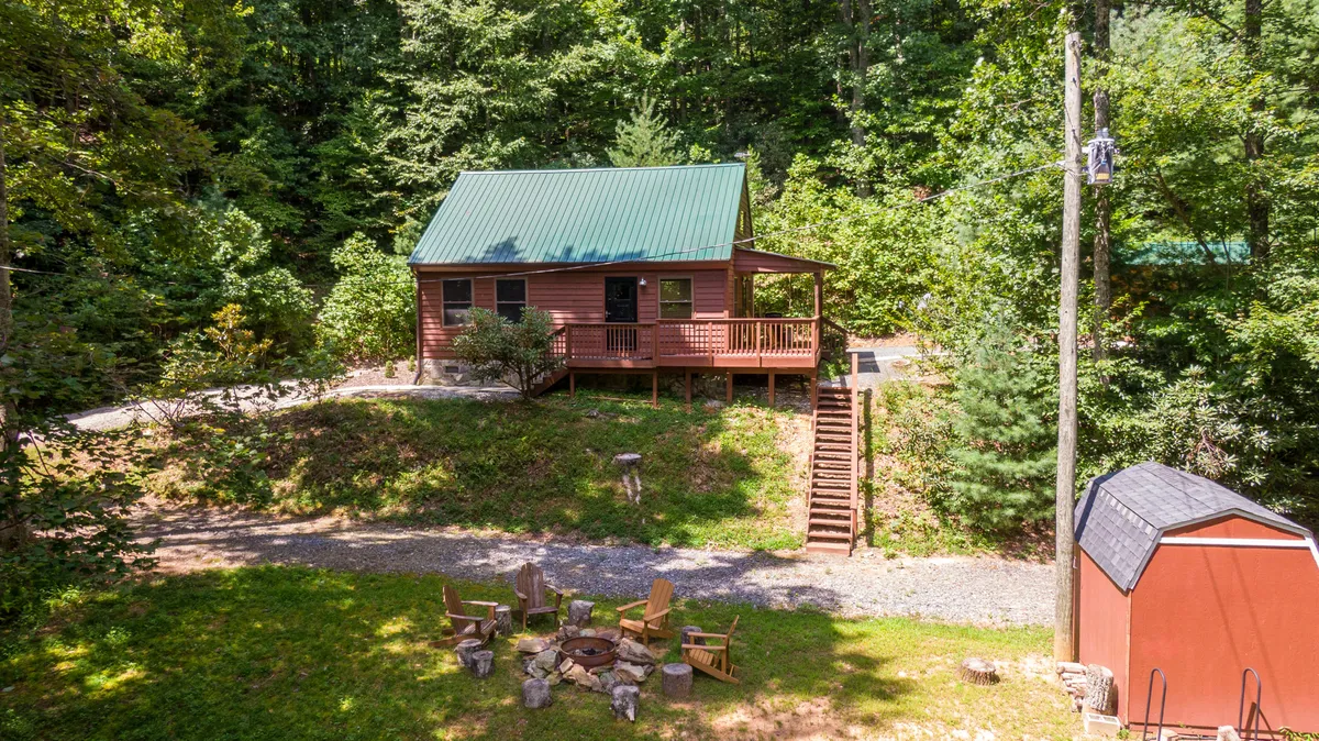The cabin set among the trees with a cozy fire pit area in the foreground. The scene suggests evenings spent relaxing outdoors, surrounded by nature, with abundant space for family or couples to gather and enjoy the peaceful surroundings.
