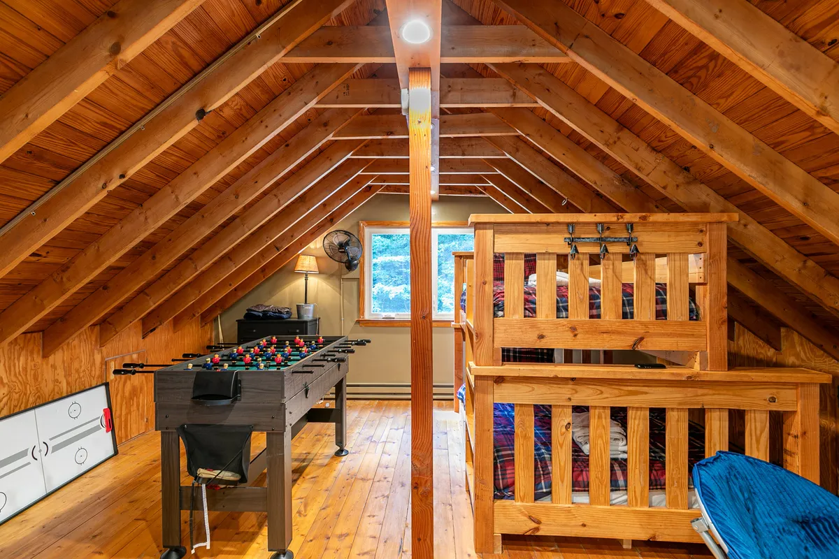 A bright, inviting loft space featuring a foosball table ready for play, with cozy bunk beds and a window streaming in natural light. The playful setup suggests hours of fun and relaxation for both kids and adults.